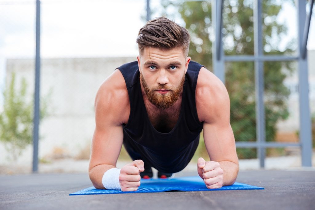 Sportsman doing plank exercise on blue fitness mat during workout